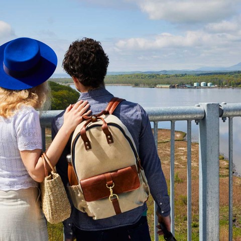 Woman in a blue hat and man with a backpack standing on the Rip Van Winkle Bridge looking at the Hudson River
